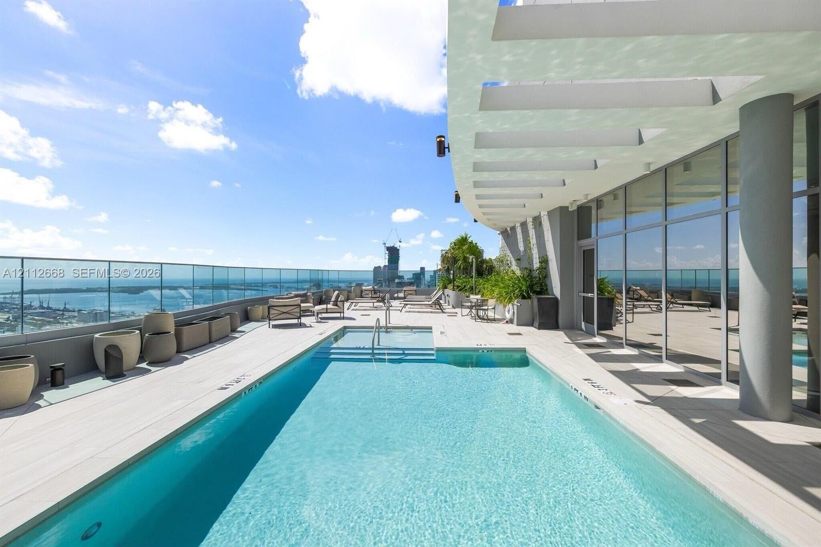 Rooftop terrace featuring an in-ground swimming pool, glass paneled perimeter fencing, expansive stone-finish decking, and a structural concrete overhang