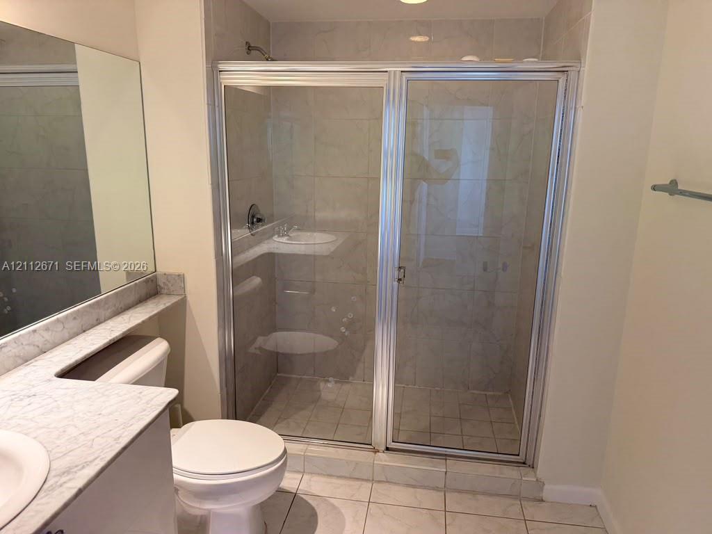 Bathroom featuring a vanity with a stone-top counter, a large wall-mounted mirror, a tiled floor, and a shower enclosure with a glass door and metal trim