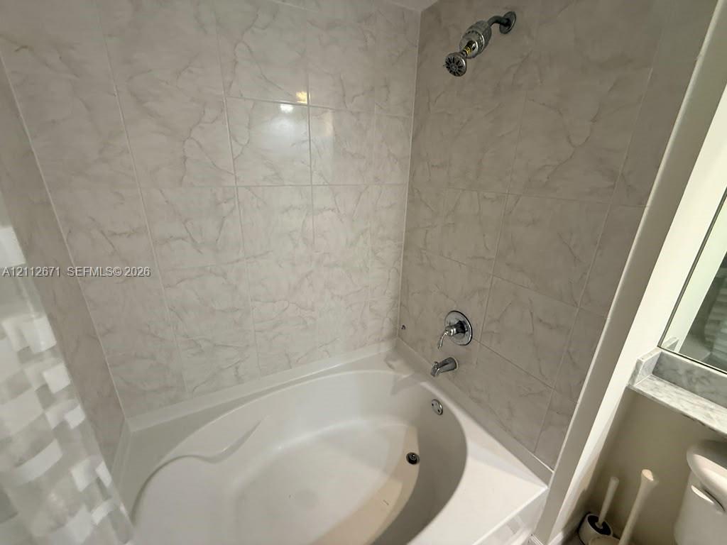 Oval soaking tub featuring light-toned tile surround, polished metal shower fixtures, and integrated ledge shelving
