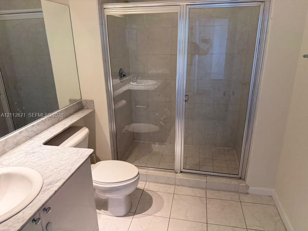 Bathroom featuring a vanity with a patterned stone-finish countertop, undermount sink, large-format tile flooring, and a walk-in shower with a glass enclosure and metal framing