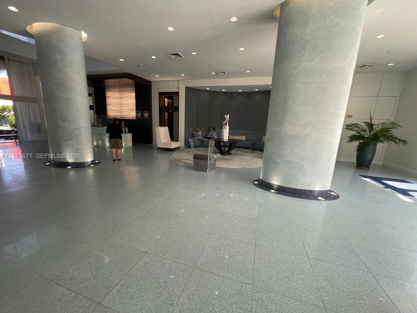 Grand lobby featuring polished stone flooring, dual floor-to-ceiling structural columns, recessed ceiling lighting, and a built-in reception desk