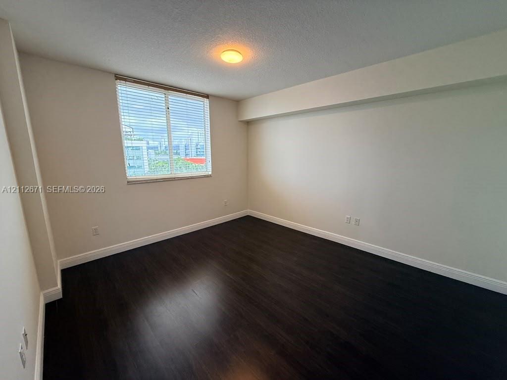 Room featuring dark wood-finish flooring, neutral wall tones, and a large window with horizontal blinds Room featuring dark wood-finish flooring, neutral wall tones, and a large window with horizontal blinds
