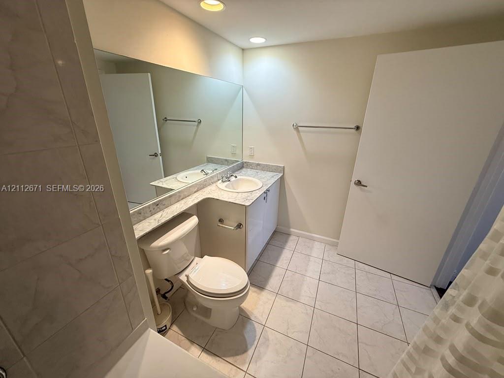Vanity featuring a stone-patterned countertop and undermount sink, complemented by a full-width wall mirror, tile flooring, and recessed ceiling lighting