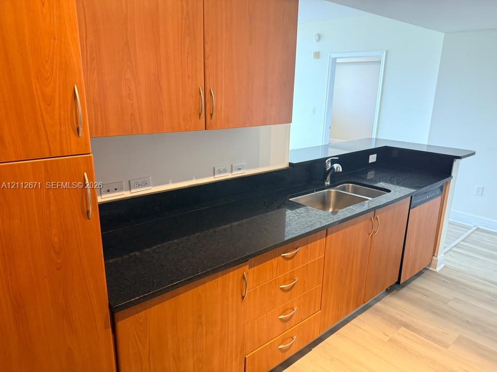 Kitchen featuring wood-finish cabinetry, dark stone countertops, stainless steel dual-basin sink, and integrated dishwasher