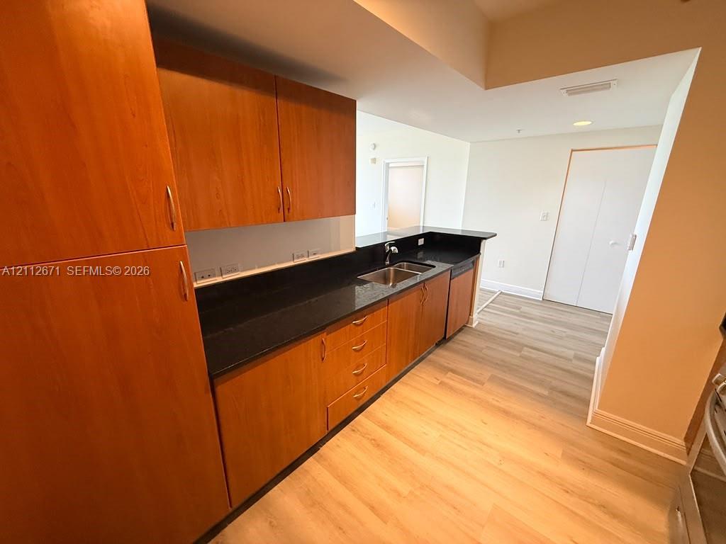 Kitchen featuring wood-finish cabinetry, dark solid-surface countertops, a stainless steel dual-basin sink, and light-toned wood-finish flooring