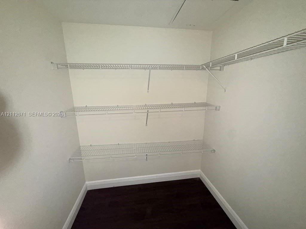Storage space featuring three levels of white wire shelving and dark wood-finish flooring