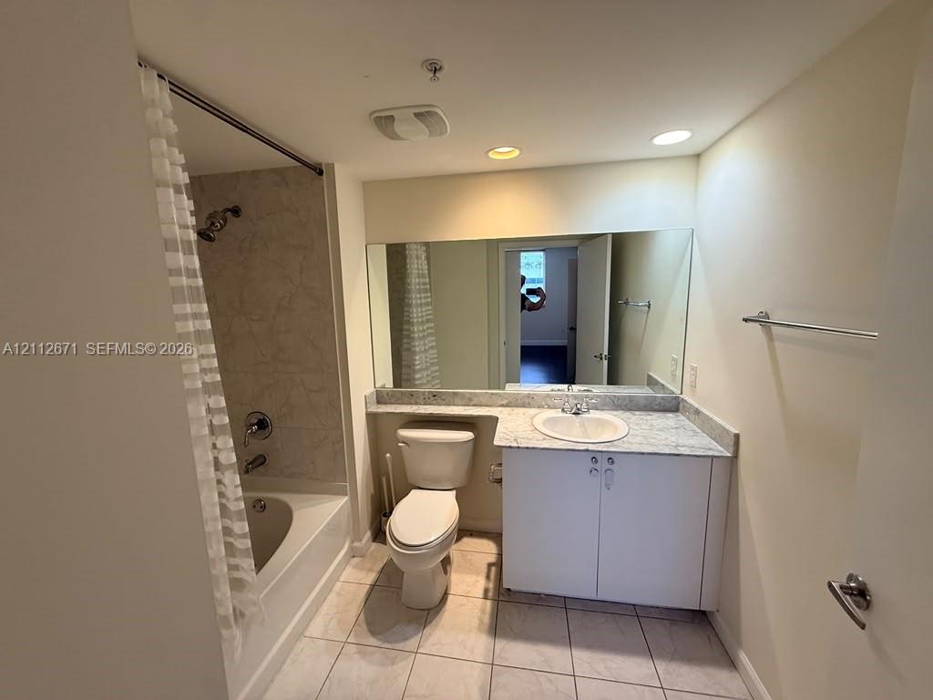 Full-width wall mirror, vanity with stone-surface countertop, integrated basin, tile flooring, and tub-shower combination with tiled surround