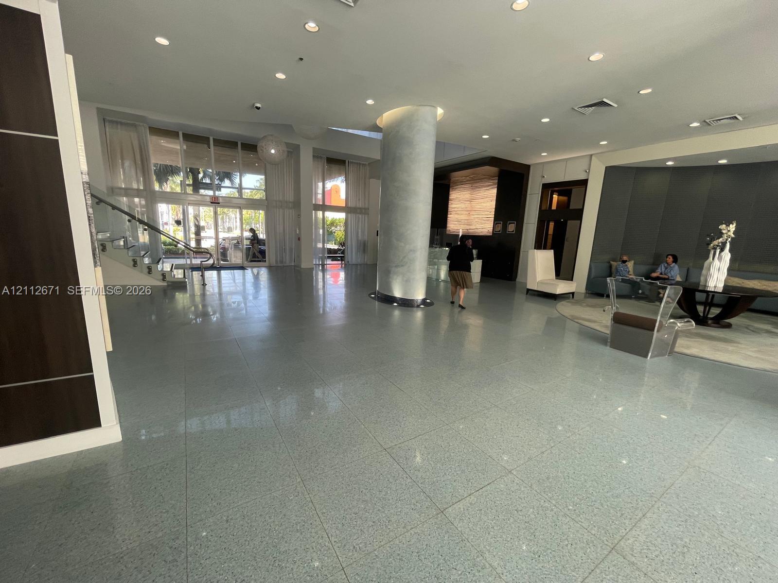 Expansive lobby featuring polished stone flooring, a floor-to-ceiling support column with a high-gloss finish, multi-panel floor-to-ceiling windows, and recessed lighting