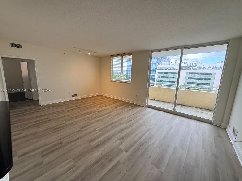 Living area featuring wood-finish flooring, sliding glass doors to a private balcony, multi-directional track lighting, and neutral-toned walls Living area featuring wood-finish flooring, sliding glass doors to a private balcony, multi-directional track lighting, and neutral-toned walls