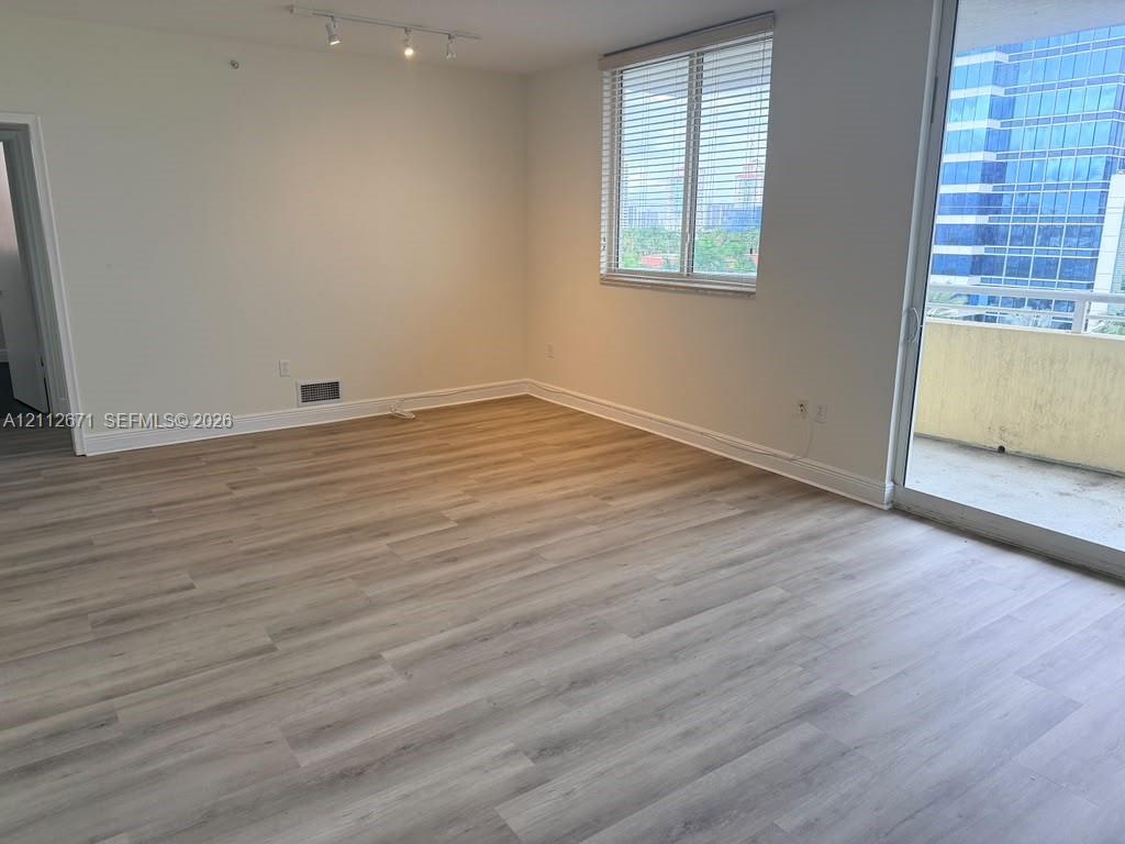 Open-concept room featuring wood-finish flooring, a glass sliding door to a balcony, track lighting, and a window with horizontal blinds Open-concept room featuring wood-finish flooring, a glass sliding door to a balcony, track lighting, and a window with horizontal blinds