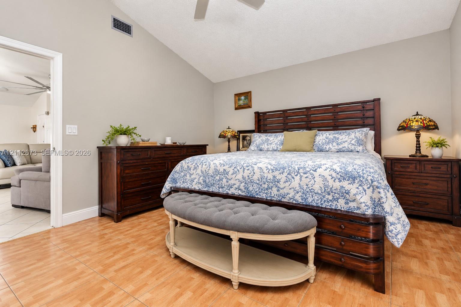 Vaulted ceiling with a central paddle fan, neutral wall paint, and wood-finish tile flooring