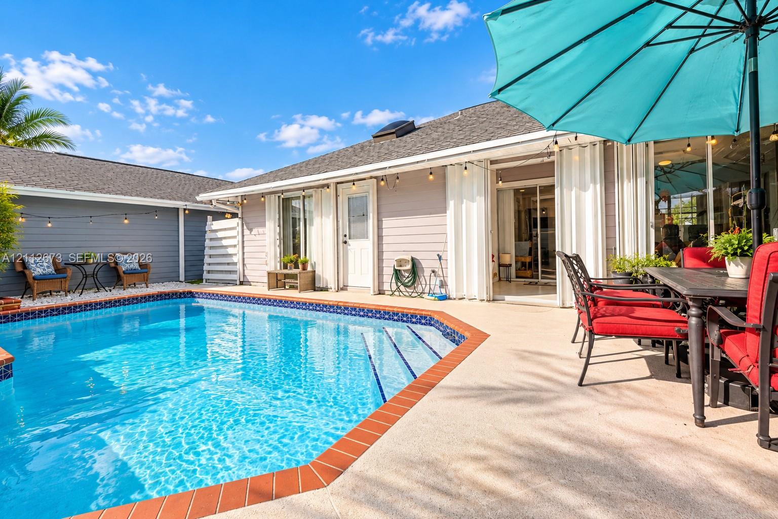 Outdoor living area featuring a swimming pool with tile trim, concrete patio surfacing, horizontal lap siding, and attached string lighting Outdoor living area featuring a swimming pool with tile trim, concrete patio surfacing, horizontal lap siding, and attached string lighting