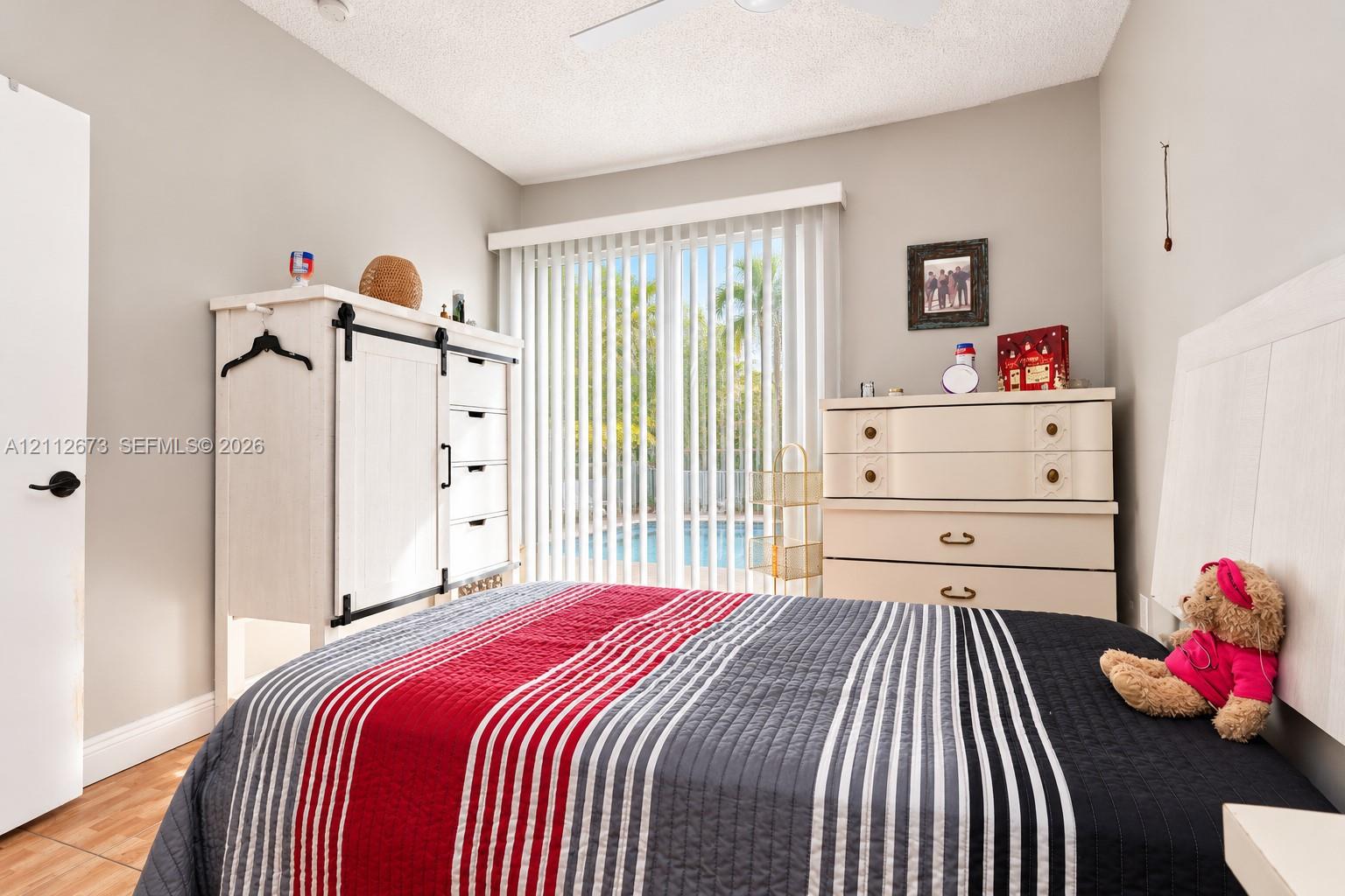 Bedroom featuring vertical sliding glass doors, neutral wall paint, tile flooring, and a ceiling-mounted fan