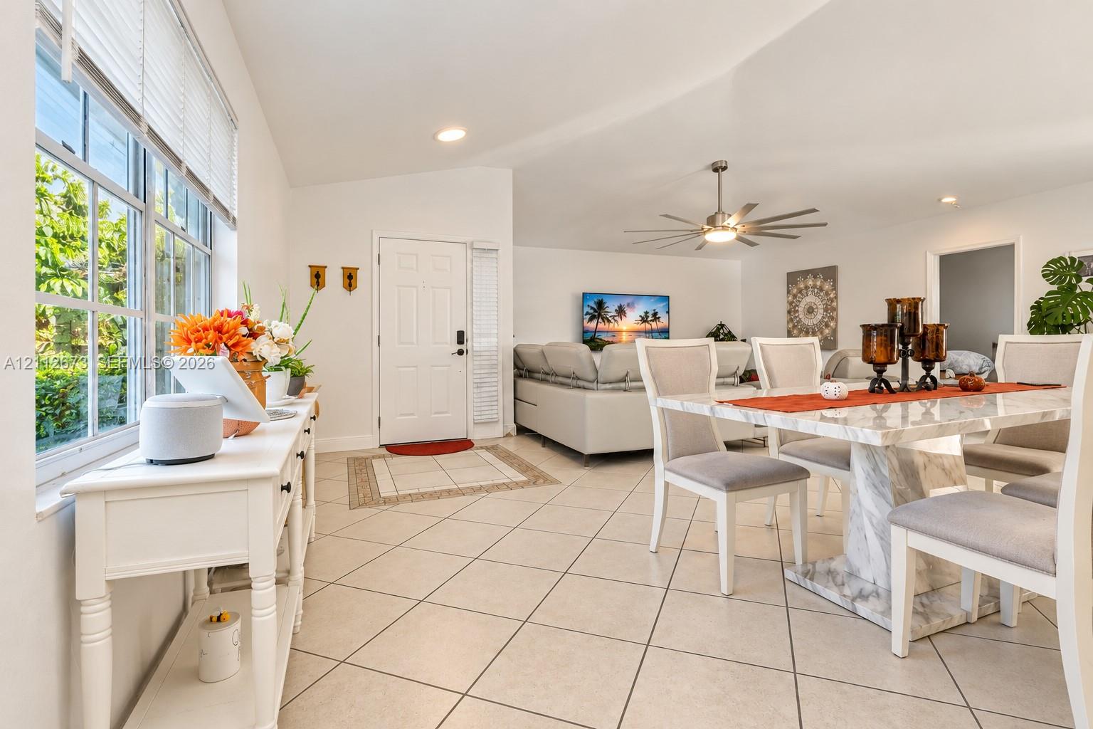 Open-concept area featuring vaulted ceilings, oversized grid-pattern windows, large-format tile flooring, and a multi-blade modern ceiling fan