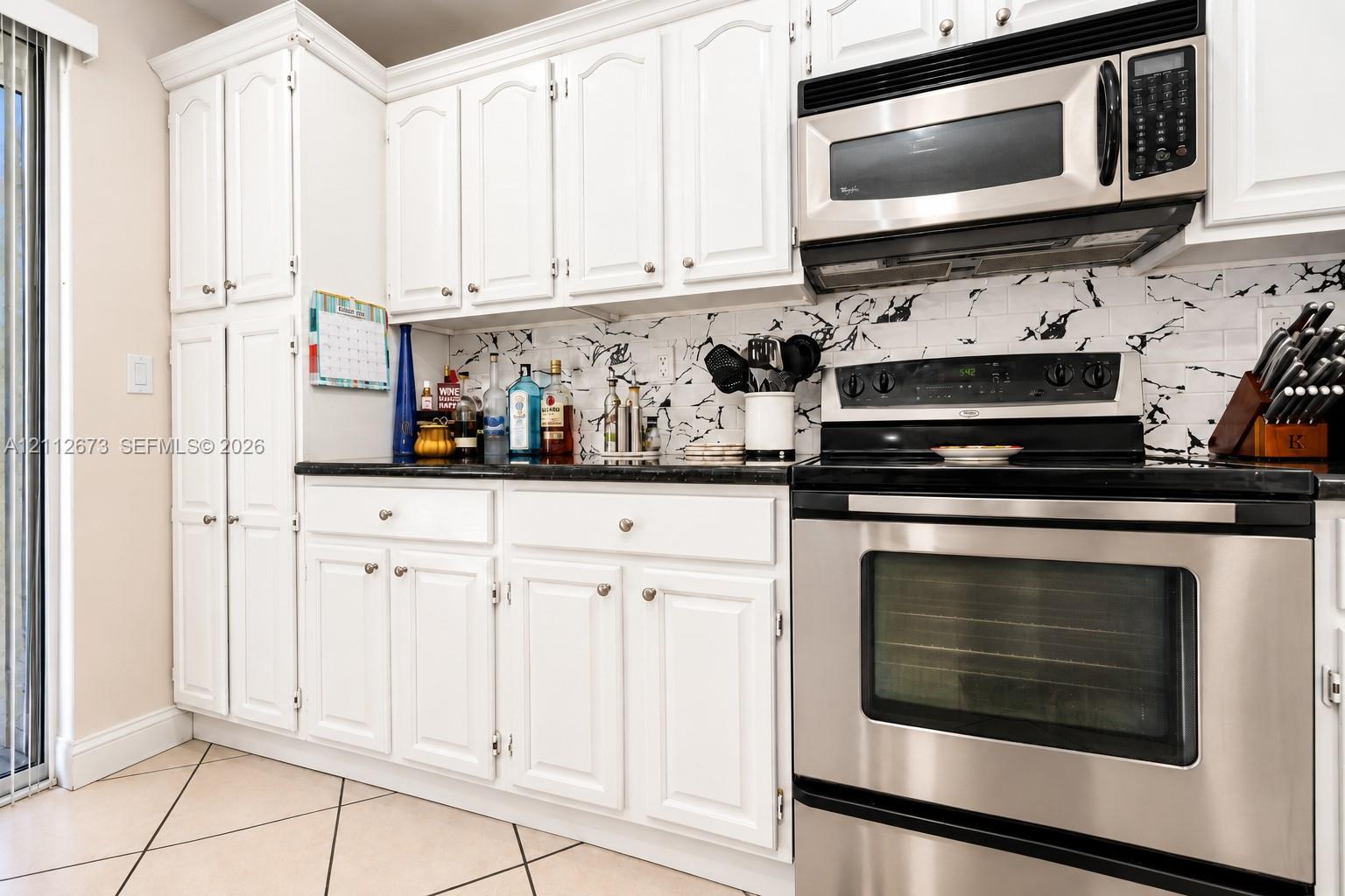 Kitchen featuring white cabinetry, dark countertops, a patterned tile backsplash, and stainless steel appliances