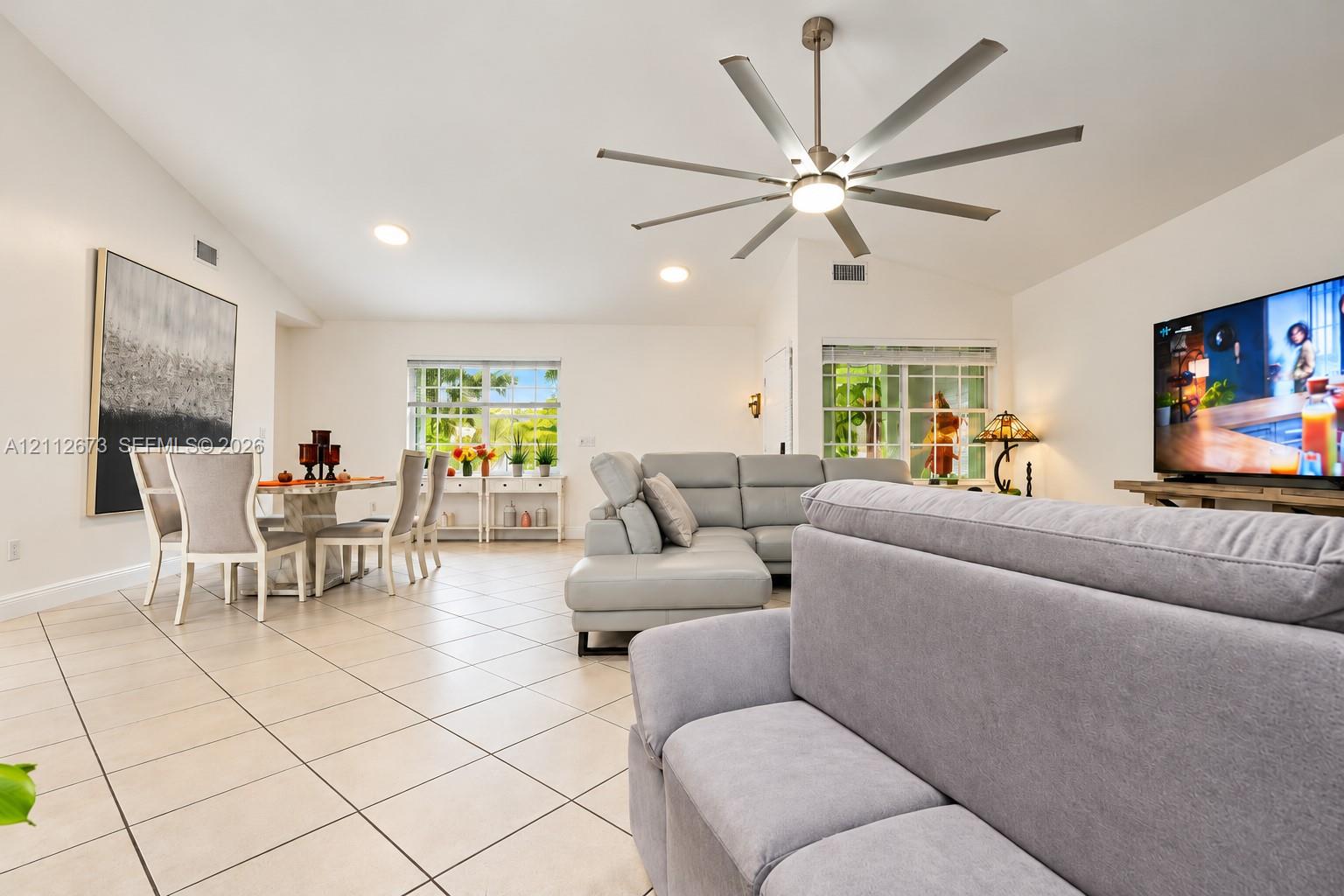 Vaulted ceilings featuring a multi-blade brushed metal ceiling fan and recessed lighting, finished with light-toned ceramic tile flooring and multi-pane windows