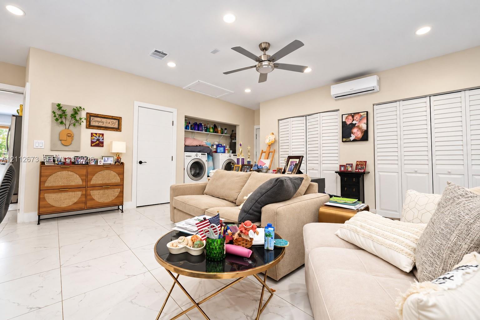Large-format tile flooring, recessed ceiling lighting, brushed metal ceiling fan, wall-mounted ductless air conditioning unit, and white louvered bifold closet doors
