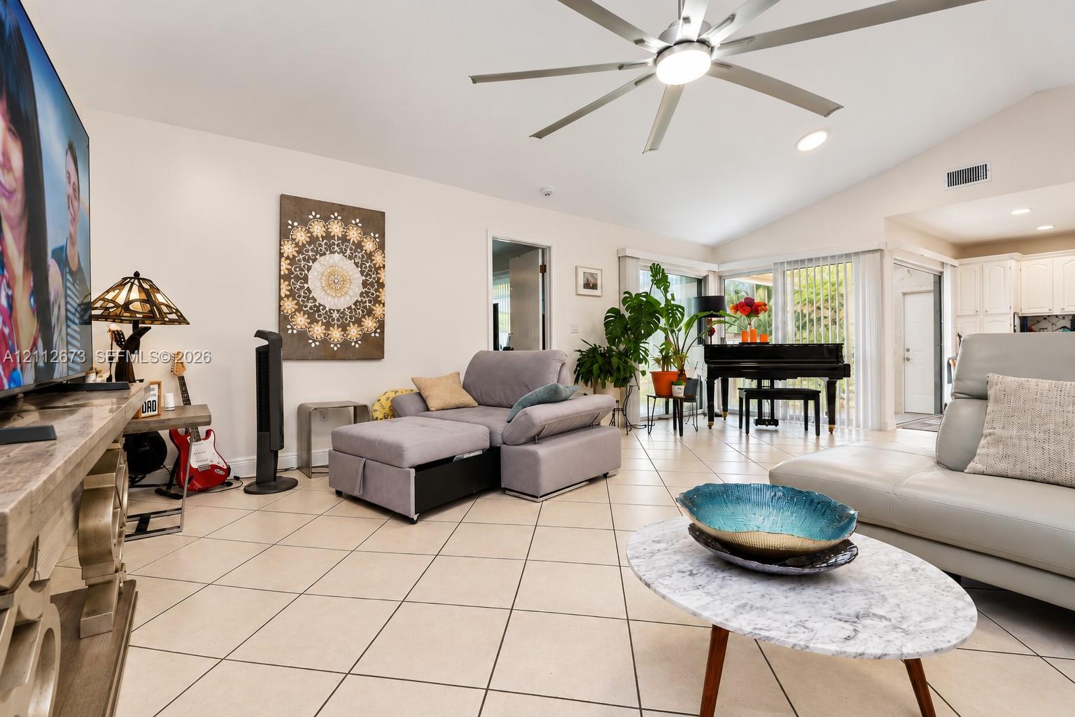 Living area featuring ceramic tile flooring, vaulted ceilings, and a large multi-blade ceiling fan with integrated lighting