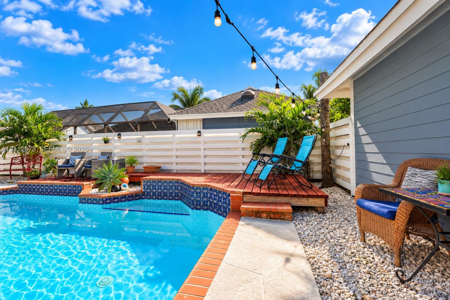 In-ground swimming pool with patterned tile border, raised wood decking, horizontal slat fencing, and stone landscape ground cover In-ground swimming pool with patterned tile border, raised wood decking, horizontal slat fencing, and stone landscape ground cover