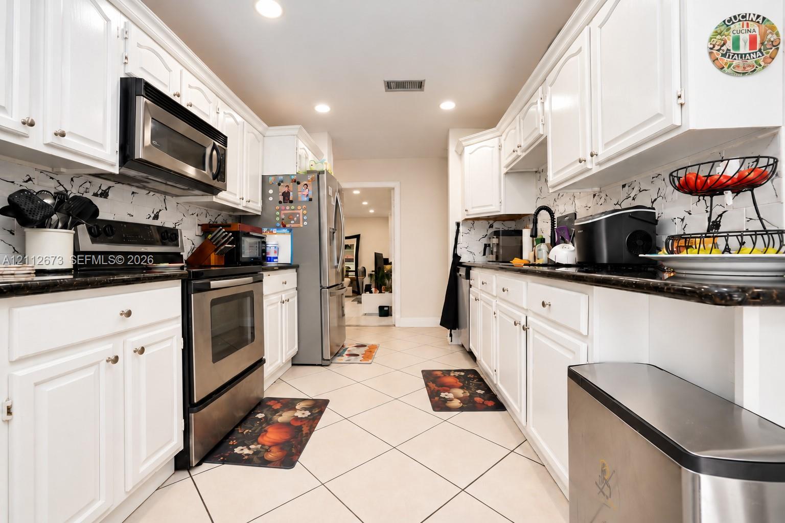 Kitchen featuring white cabinetry, dark stone-finish countertops, stainless steel appliances, marble-patterned backsplash, and recessed lighting