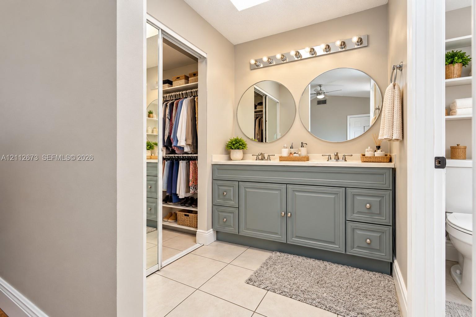 Bathroom vanity featuring a slate-toned cabinetry base, dual circular wall mirrors, a multi-bulb vanity light fixture, light-toned countertop, and sliding mirrored closet doors