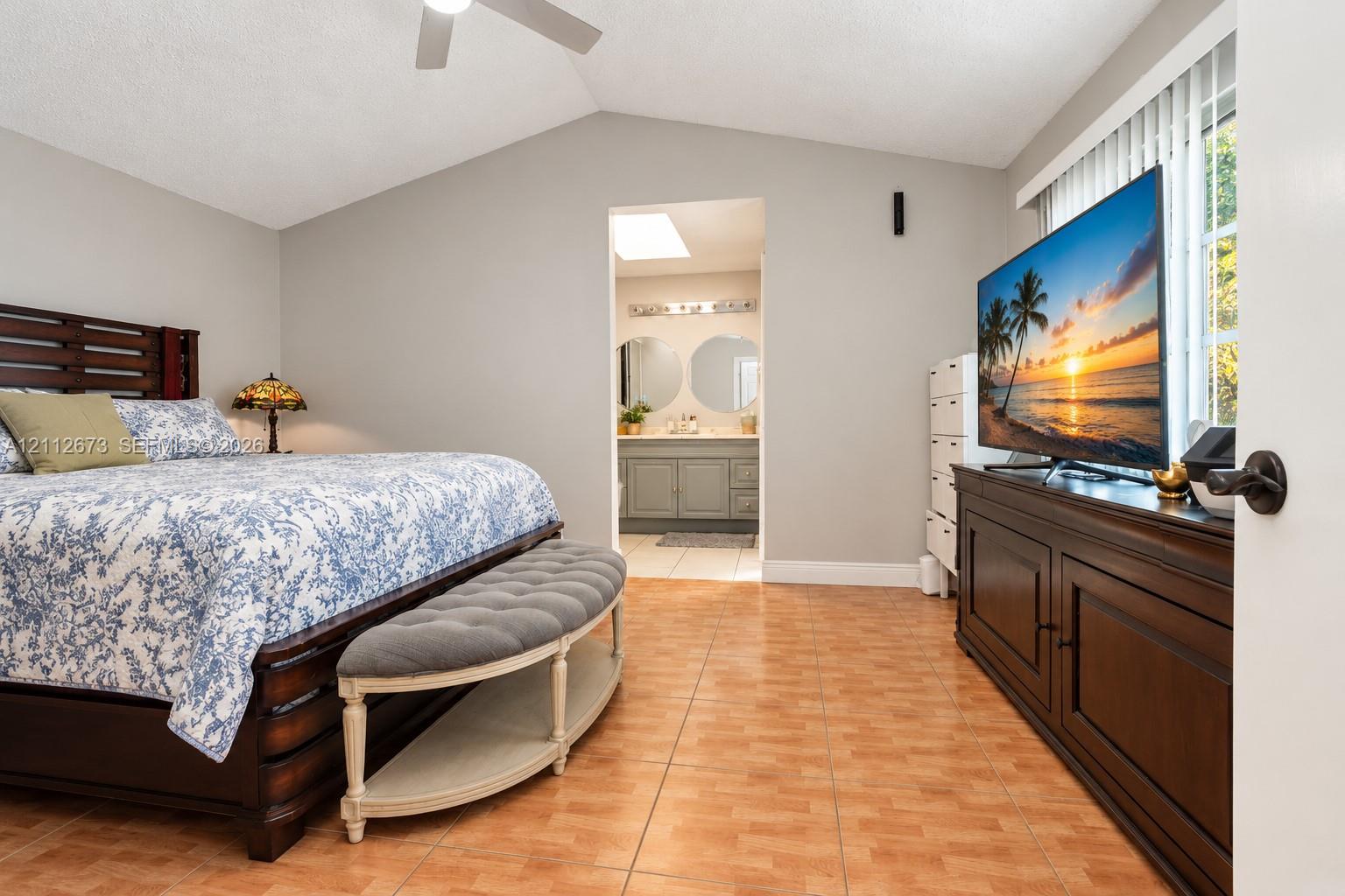 Vaulted ceiling with a central paddle fan, tile flooring, and vertical blinds