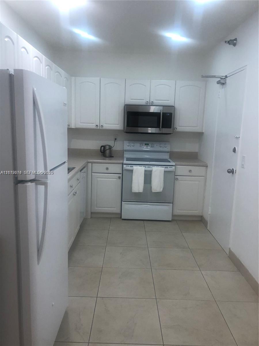 Kitchen featuring white cabinetry, solid-surface countertops, tile flooring, and stainless steel microwave and oven appliances Kitchen featuring white cabinetry, solid-surface countertops, tile flooring, and stainless steel microwave and oven appliances