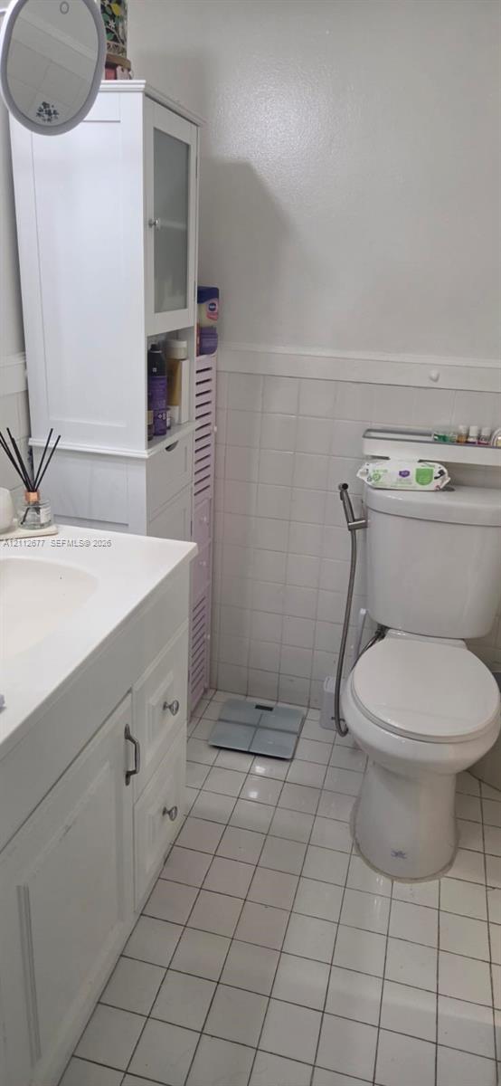 Bathroom featuring white cabinetry, a built-in vertical storage tower, square-tile flooring, tiled wainscoting, and a standard-height toilet