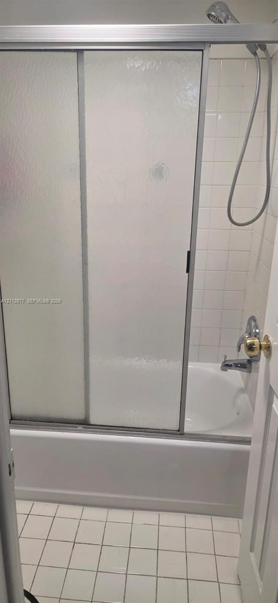 Bathtub and shower combination featuring a sliding glass enclosure, white ceramic wall tile, and a handheld shower fixture