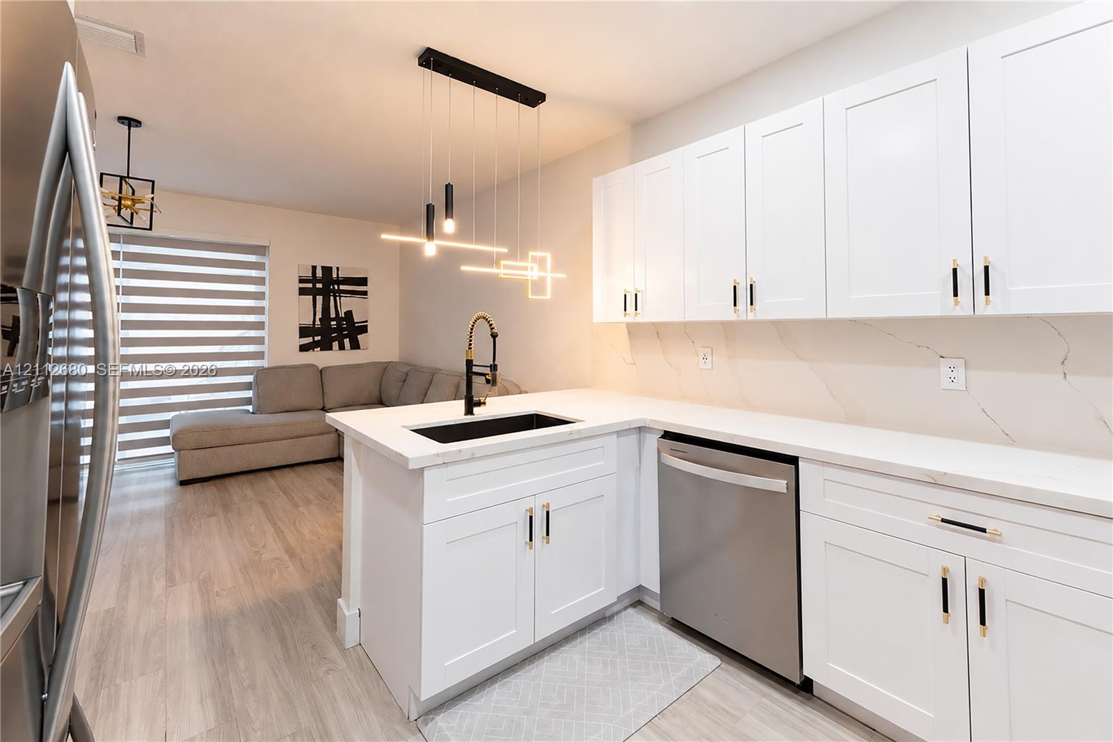 Kitchen featuring white shaker-style cabinetry, quartz countertops with integrated backsplash, matte black hardware, stainless steel dishwasher, and modern linear pendant lighting Kitchen featuring white shaker-style cabinetry, quartz countertops with integrated backsplash, matte black hardware, stainless steel dishwasher, and modern linear pendant lighting