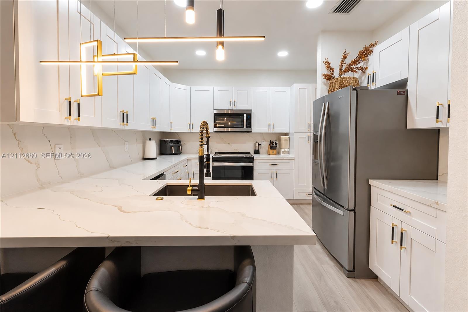 Kitchen featuring white shaker-style cabinetry, white countertops with grey veining, integrated stainless steel appliances, a pull-down faucet, and contemporary geometric pendant lighting Kitchen featuring white shaker-style cabinetry, white countertops with grey veining, integrated stainless steel appliances, a pull-down faucet, and contemporary geometric pendant lighting