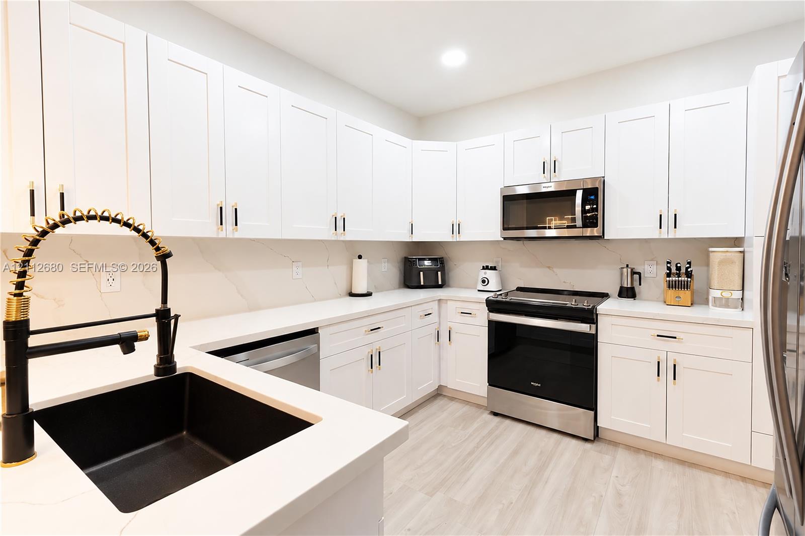 Kitchen featuring white shaker-style cabinetry, white countertops with subtle veining, undermount sink with a matte black pull-down faucet, stainless steel appliances, and wood-finish flooring Kitchen featuring white shaker-style cabinetry, white countertops with subtle veining, undermount sink with a matte black pull-down faucet, stainless steel appliances, and wood-finish flooring