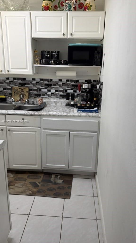 Kitchen featuring white cabinetry, stone-patterned laminate countertops, and a multi-toned mosaic tile backsplash