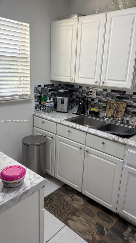 Kitchen area featuring white cabinetry, stone-patterned laminate countertops, double-basin stainless steel sink, and a decorative mosaic tile backsplash