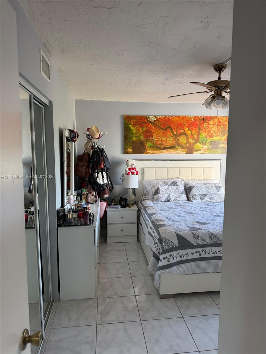 Room featuring light-toned tile flooring, dual sliding-mirror closet doors, and a ceiling fan with integrated lighting