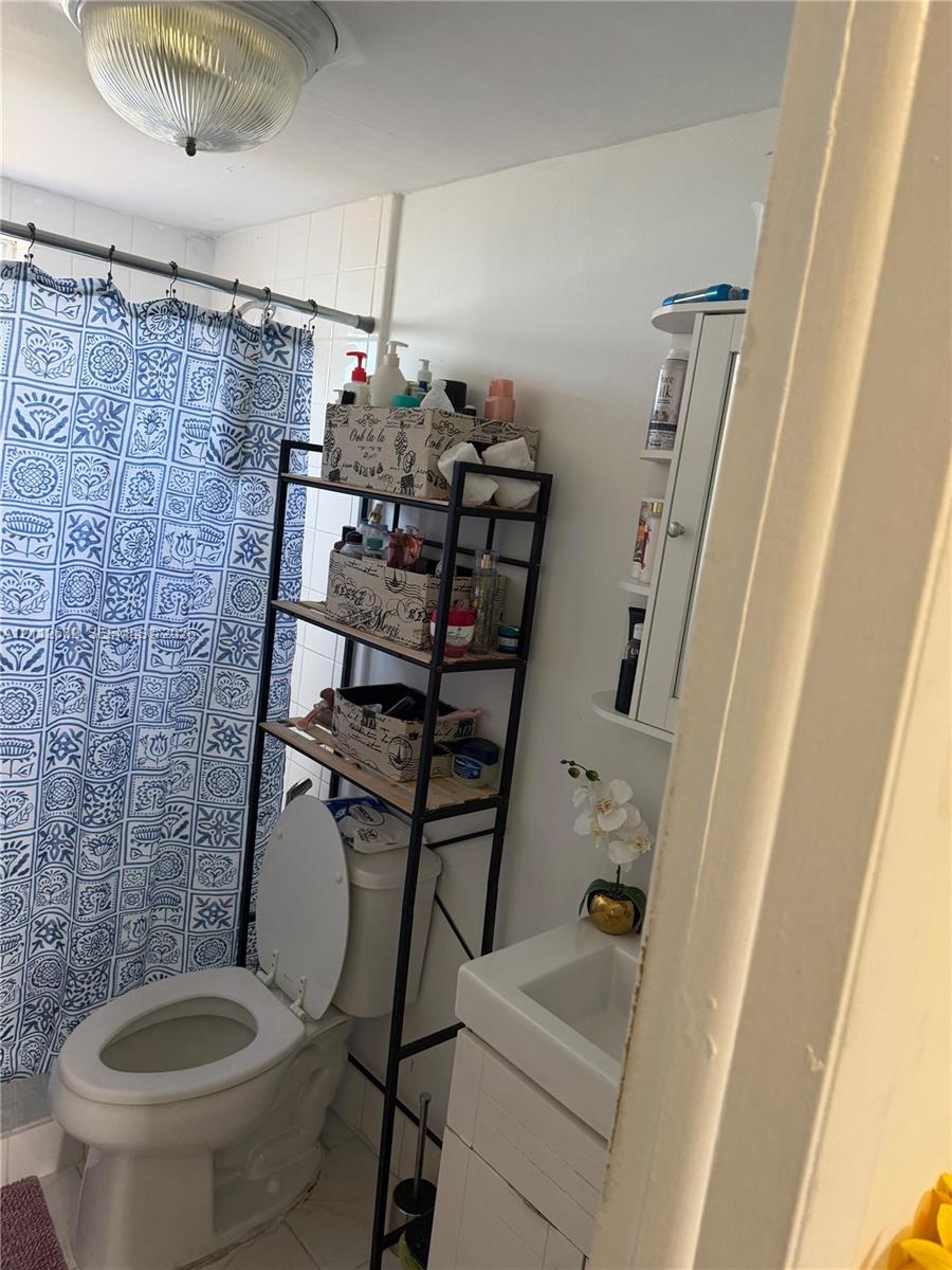 Bathroom featuring a white vanity cabinet, ceramic sink, wall-mounted white storage shelving, and a flush-mount dome light fixture