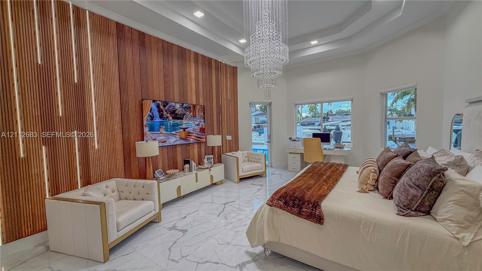 Tray ceiling with recessed lighting, large crystal chandelier, vertical wood slat accent wall with integrated LED lighting, and polished stone-finish flooring