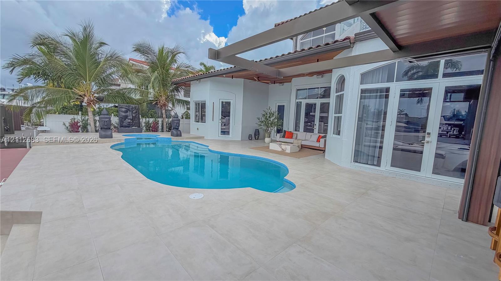 Outdoor patio featuring large-format tile flooring, a custom swimming pool with built-in spillway, a covered pergola structure, and expansive glass paneled doors