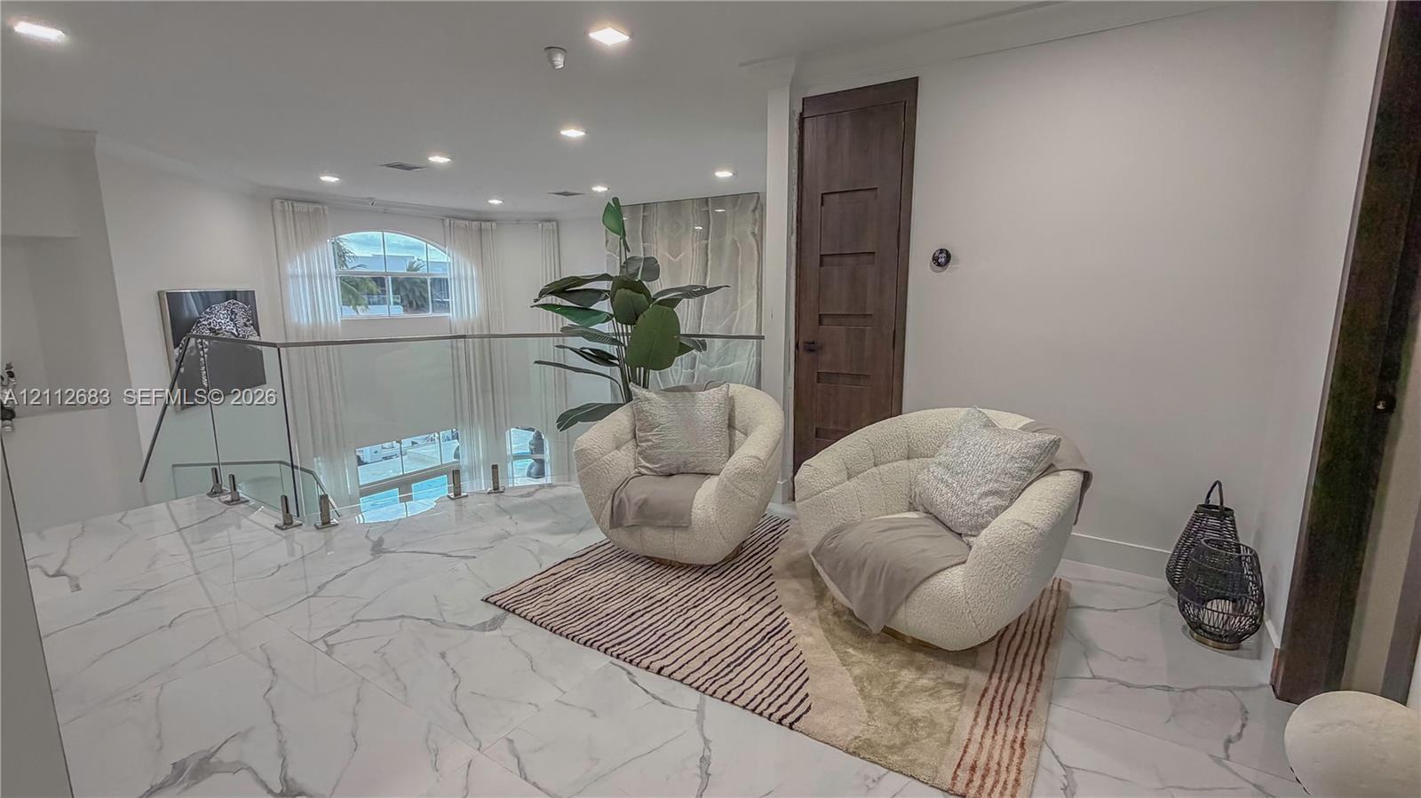 Polished stone-finish flooring with veining, glass panel railing with stainless steel standoffs, recessed ceiling lighting, and a dark wood-finish five-panel interior door