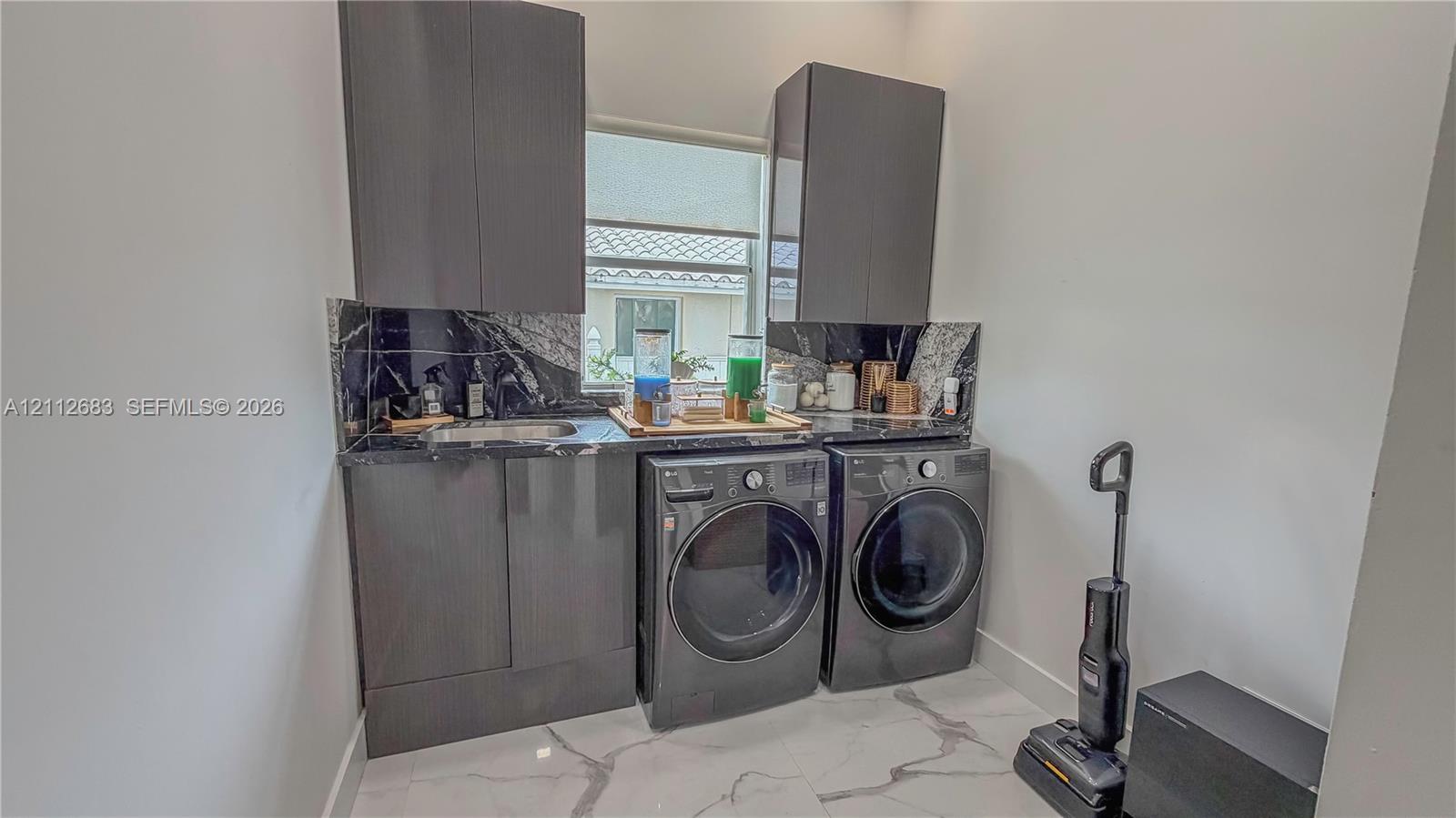 Dark wood-finish cabinetry, stone-look backsplash, built-in stainless steel sink, and large-format tile flooring