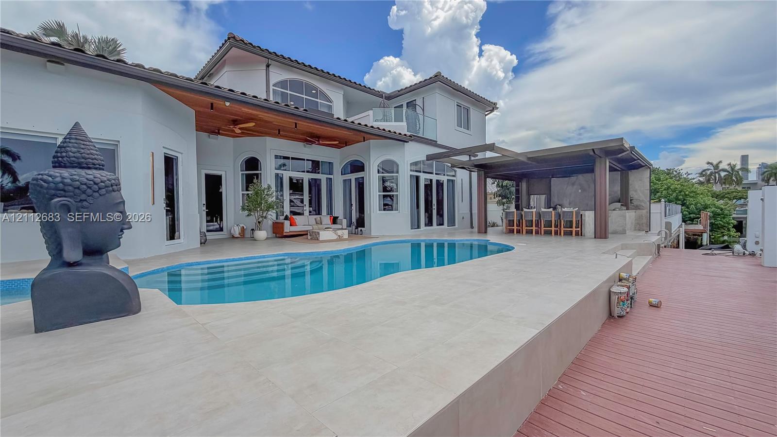 Exterior featuring a swimming pool, covered outdoor kitchen with bar seating, wood-tone decking, and a second-story balcony