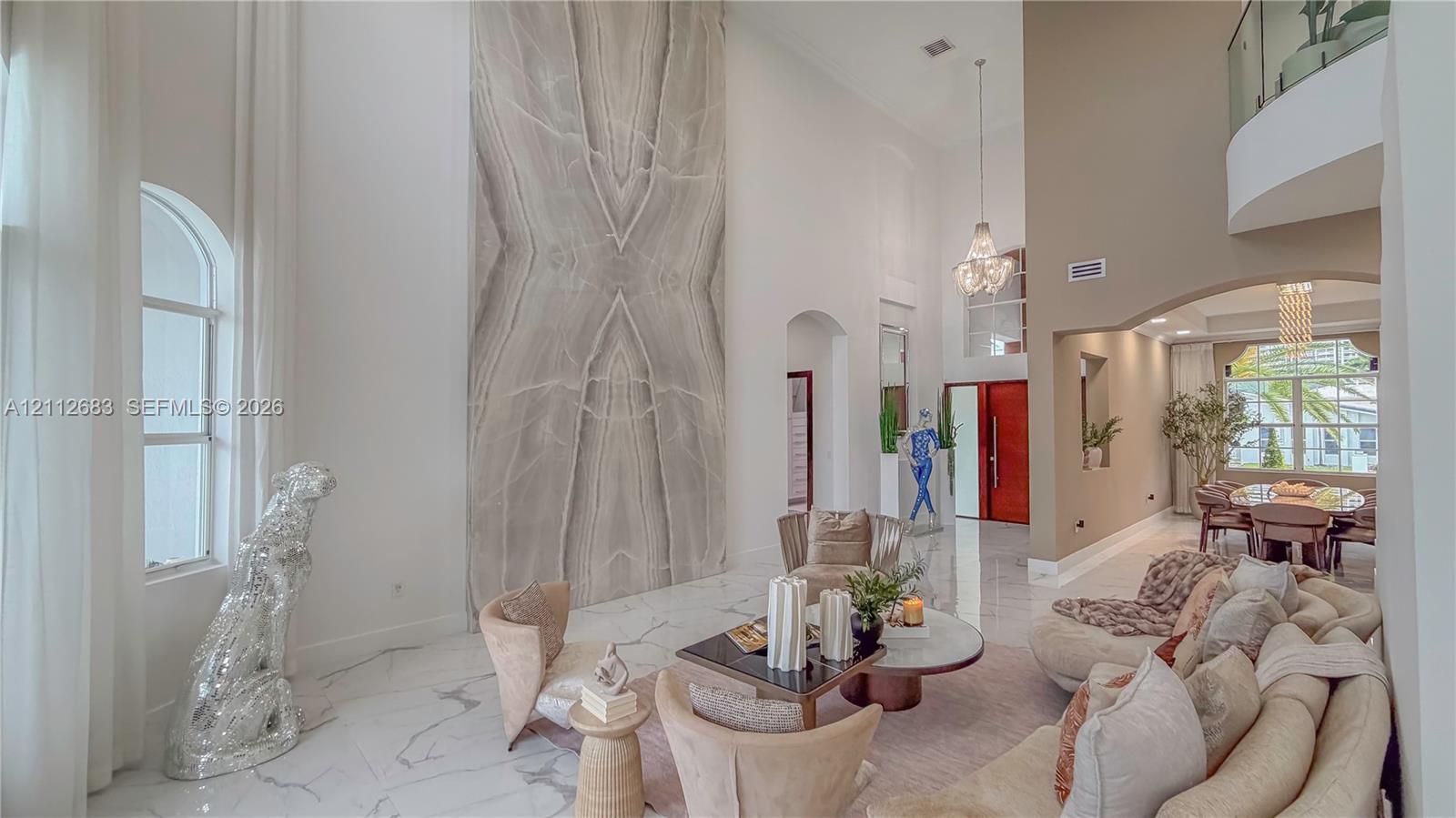 Double-height ceiling, floor-to-ceiling stone-cladding feature wall, polished stone flooring, glass-railing gallery, and tiered crystal chandelier
