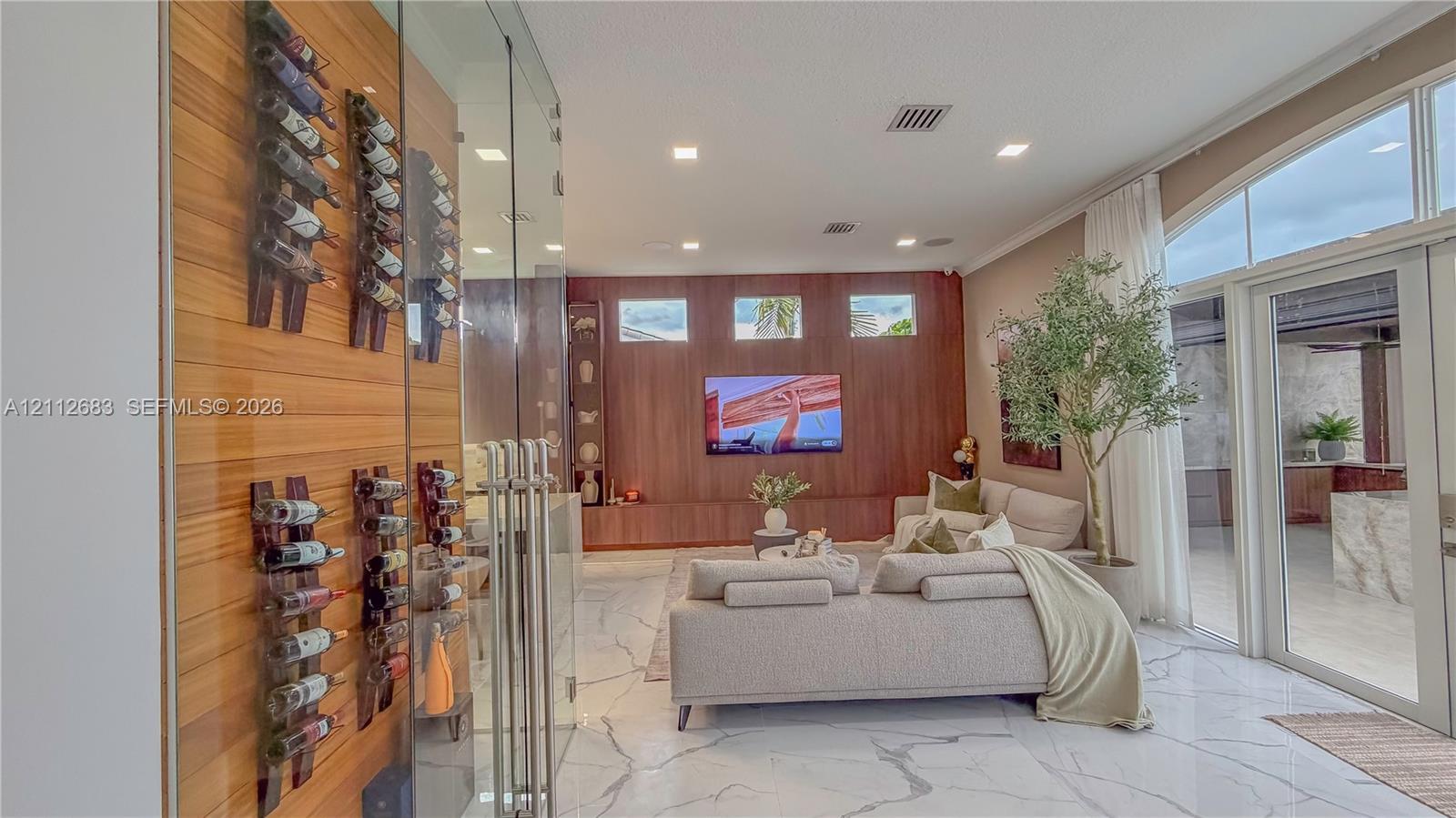 Custom floor-to-ceiling glass-enclosed wine storage featuring wood-paneled walls and wall-mounted racking, polished stone tile flooring, and wood-paneled accent wall with integrated cabinetry