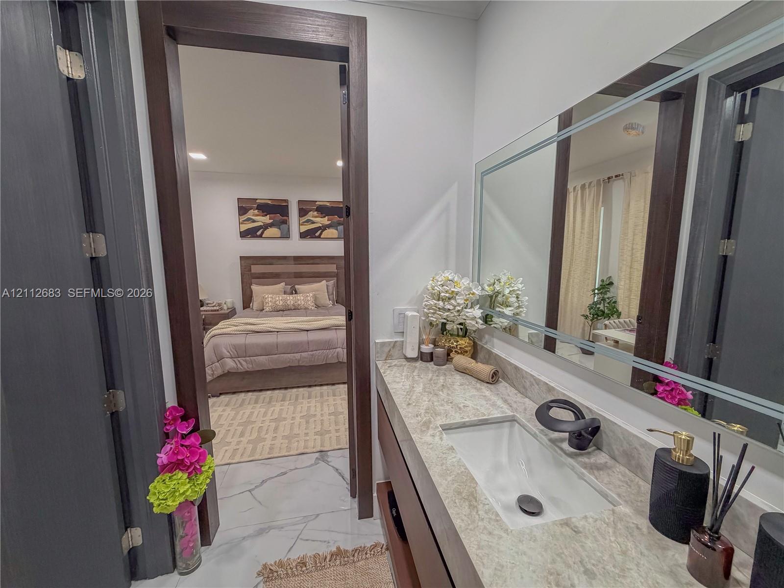 Vanity featuring a rectangular undermount sink, stone countertop, matte black faucet, and a large framed mirror with integrated lighting