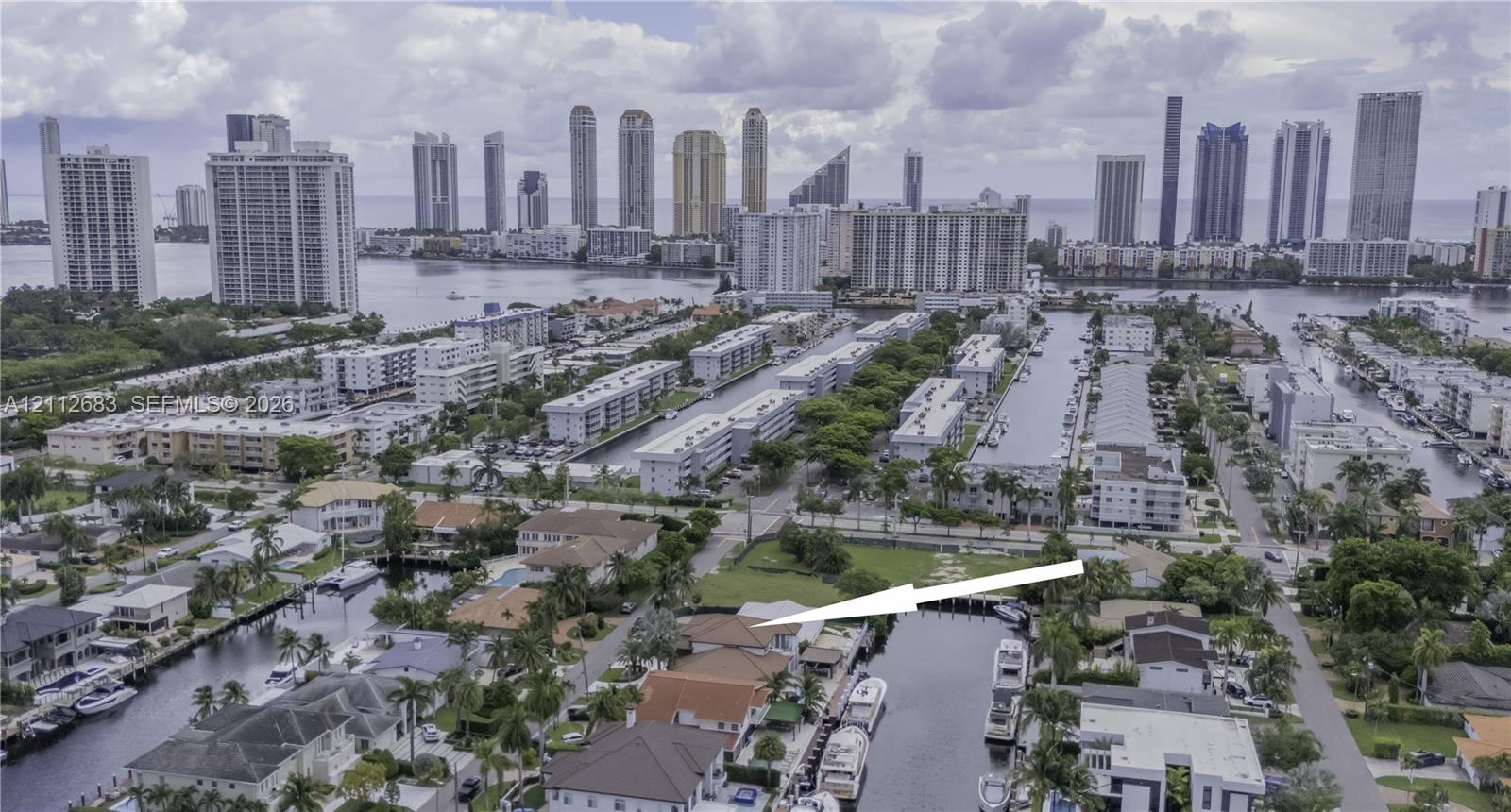 Aerial perspective of a waterfront property featuring direct canal access, a private boat slip, a multi-pitched roofline, and proximity to an urban skyline Aerial perspective of a waterfront property featuring direct canal access, a private boat slip, a multi-pitched roofline, and proximity to an urban skyline