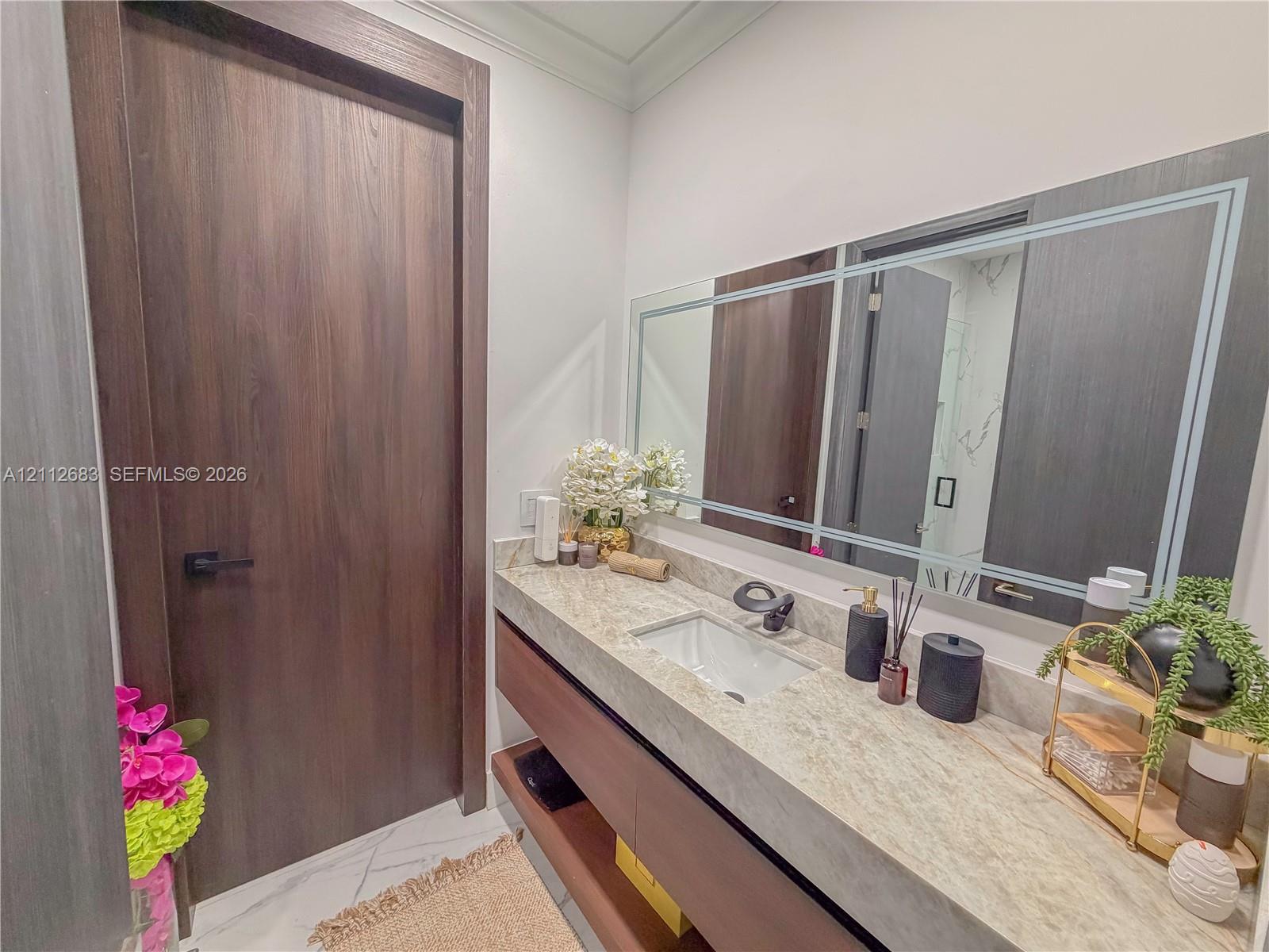 Floating vanity featuring a natural stone countertop, rectangular undermount sink, matte black faucet, and large-format wall mirror with decorative inlay
