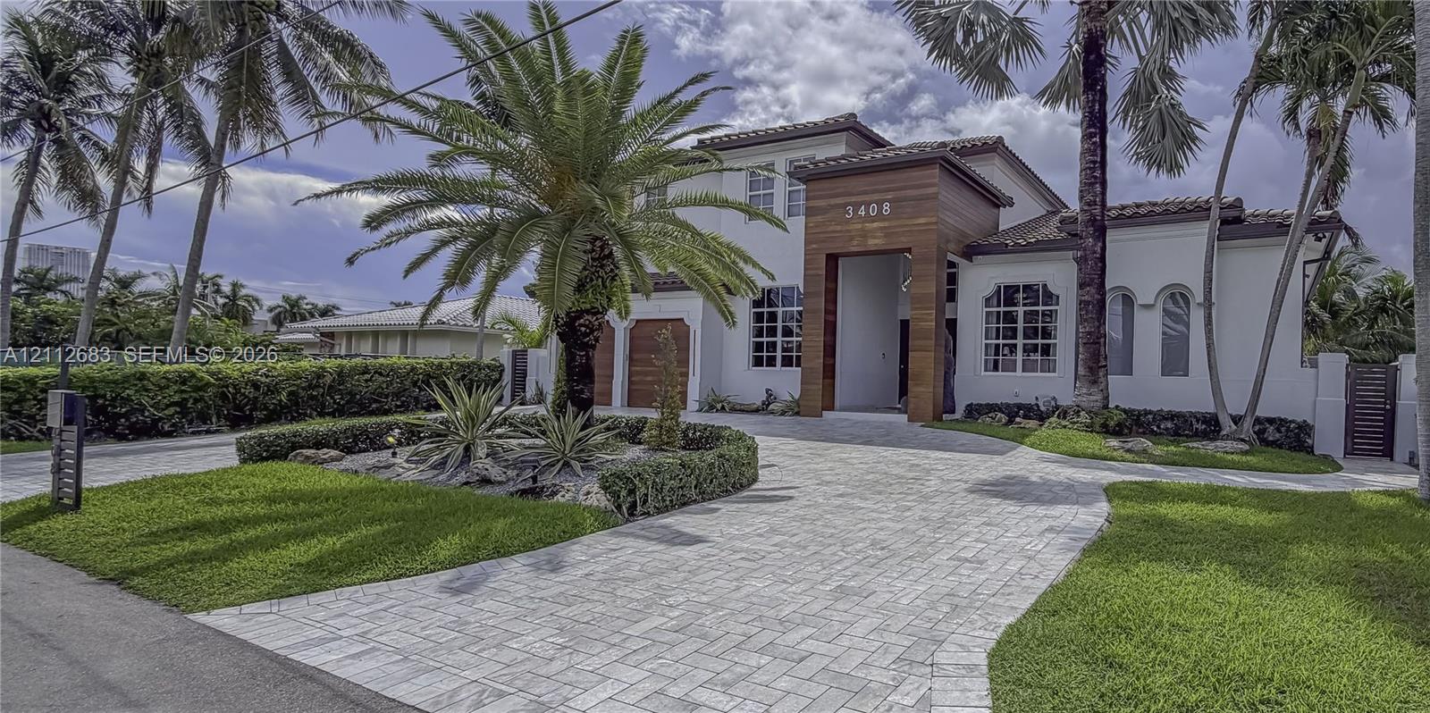 Two-story exterior featuring white stucco finish, wood-plank architectural accents, paver driveway, arched windows, and manicured landscaping