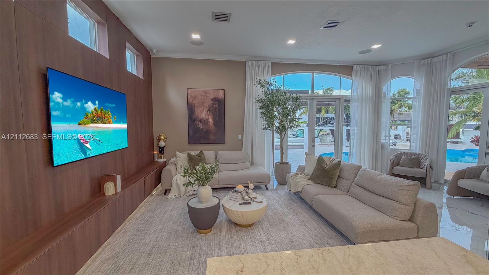 Living space featuring wood-finish accent wall paneling, large-format tile flooring, recessed lighting, and arched glass doors
