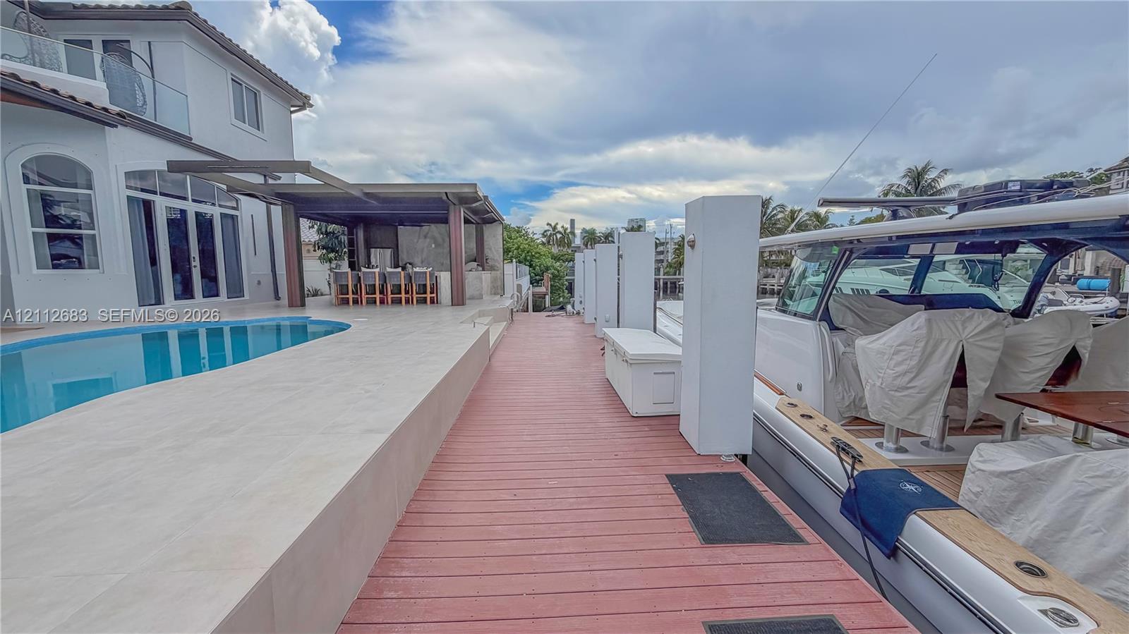 Waterfront exterior featuring a private boat dock, a tiled pool deck, an in-ground swimming pool, and a covered outdoor bar area