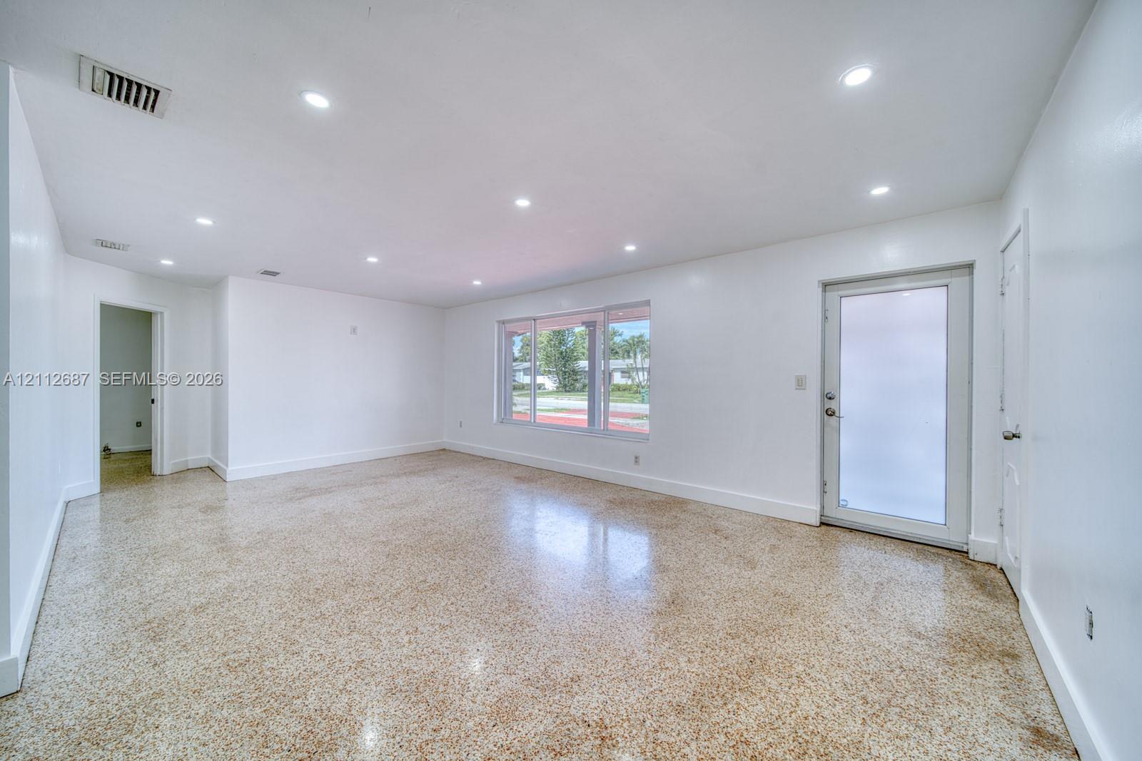 Spacious room featuring polished terrazzo flooring, recessed lighting, and a glass-paneled exterior door